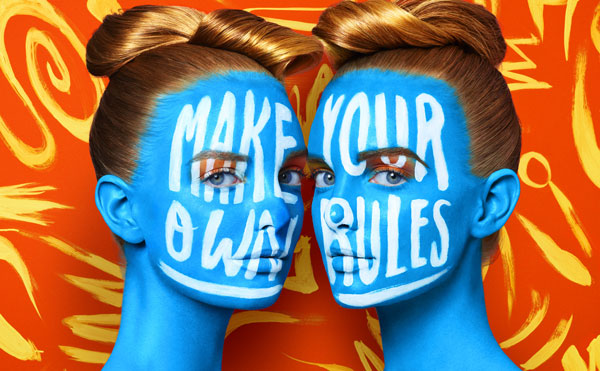 Two women's faces painted blue with "Make your own rules" painted across their faces