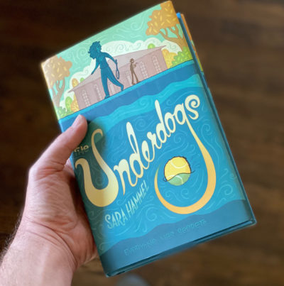 Left hand holding copy of "Underdogs" by Sara Hammel