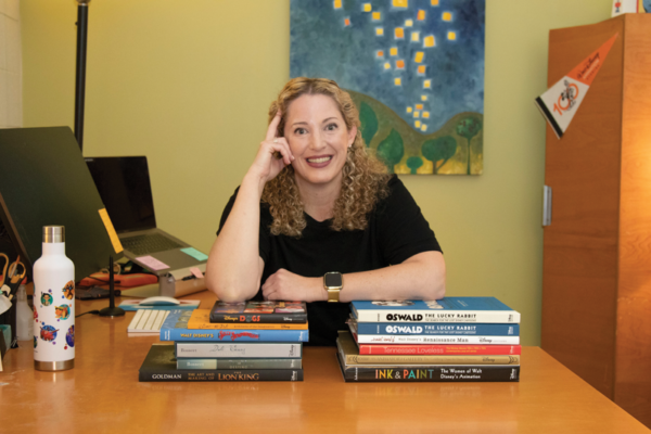 Khalaf posing at table, smiling and leaning on two piles of books totalling 12 titles