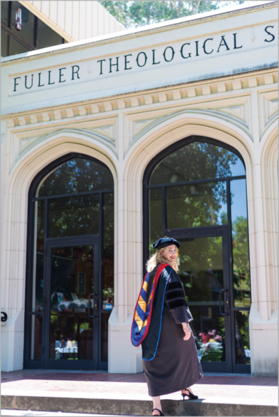 Woman entering building with "Fuller Theological" sign on Renaissance Revival style building; she is dressed in academic regalia with a red, blue, and gold hood