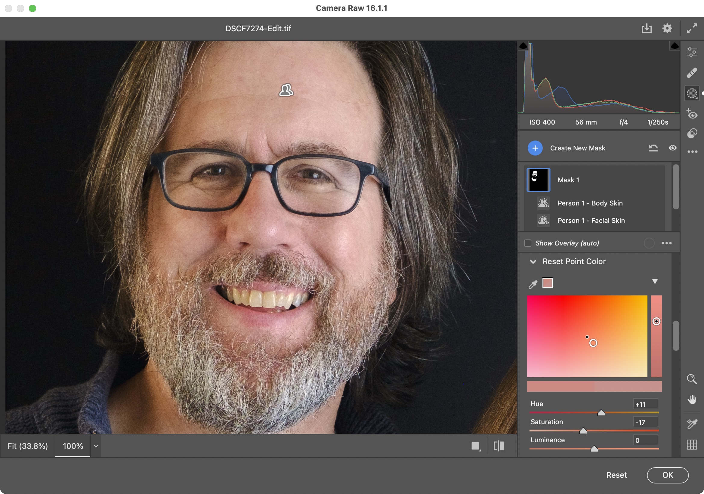 Screenshot of Adobe Camera Raw with a portrait zoomed into one person, a smiling man with a beard. The Point Color tool is being used to remove bright red portions of the man’s face.